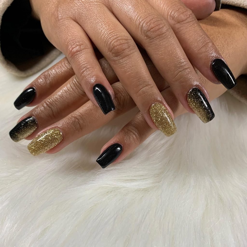 Stylish black and gold glitter ombre manicure on a soft white fur background.