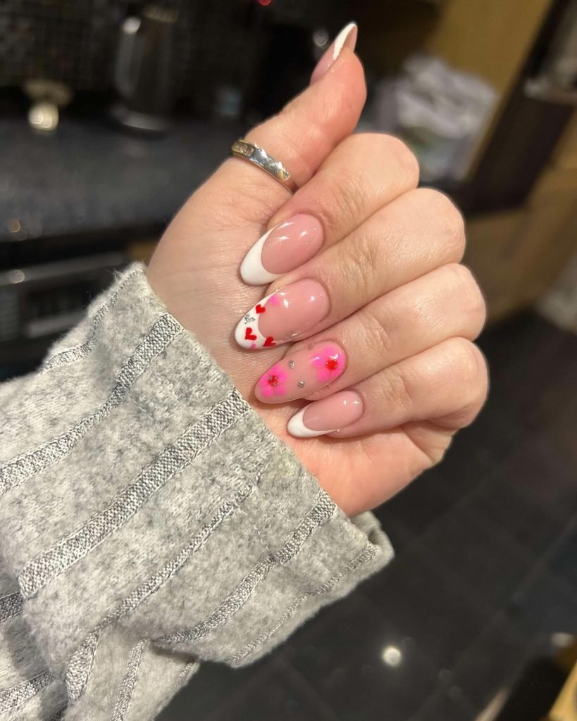 Close-up of elegant nail art with pink, white tips, hearts, and floral designs on manicured fingers.