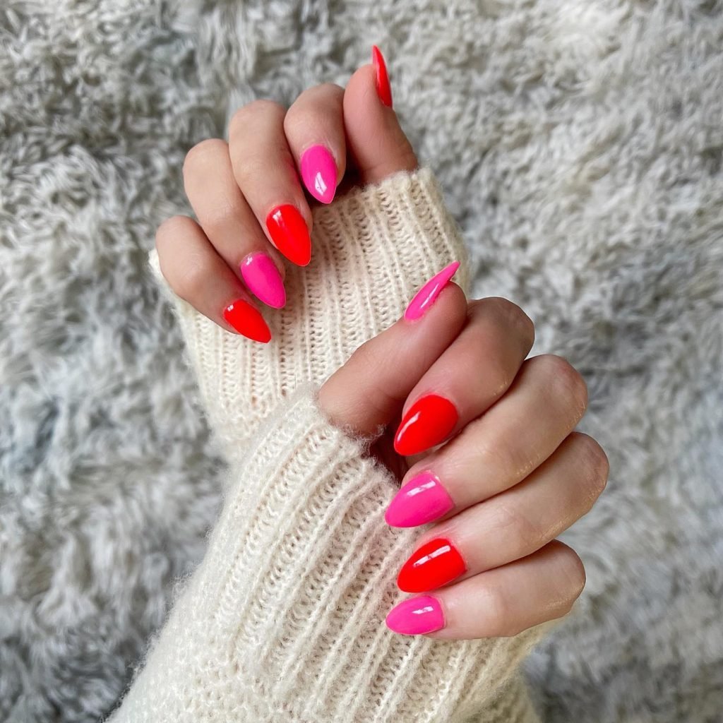 Vibrant pink and red manicure on hands in a cozy sweater against a soft, textured background.
