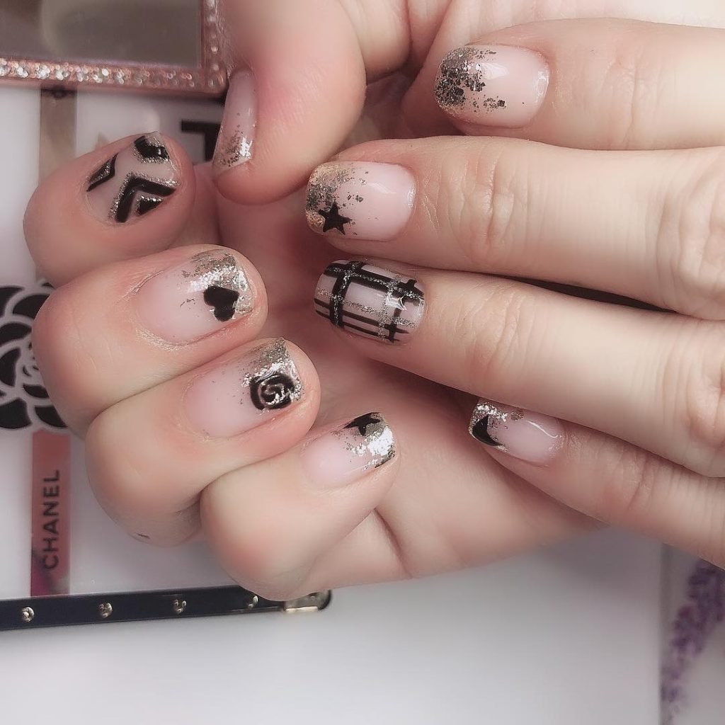 Stylish black and silver nail art with geometric and floral designs on a light pink nail base.