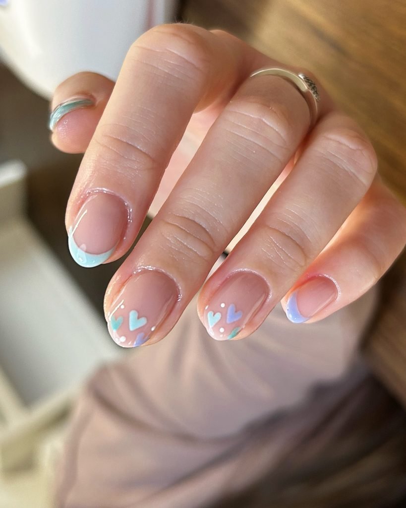Pastel heart nail art manicure with light blue and pink tips, featuring a silver ring on the index finger.