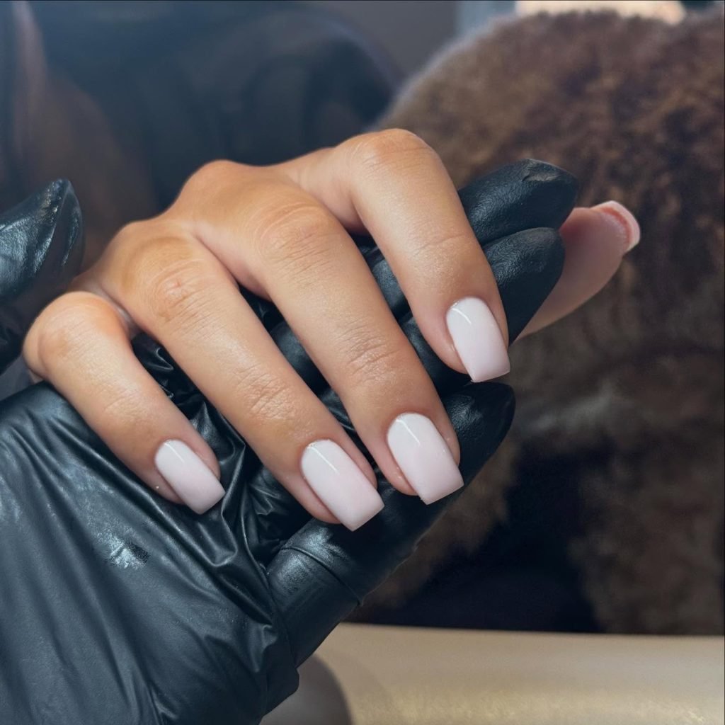 Manicure with elegant nude nails held by a gloved hand, showcasing a polished nail art design.
