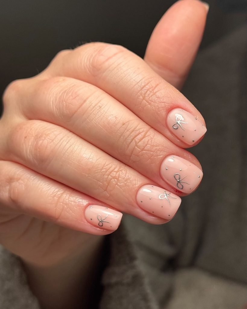 Elegant short nails with delicate bow nail art on nude polish for a chic, minimalist look.