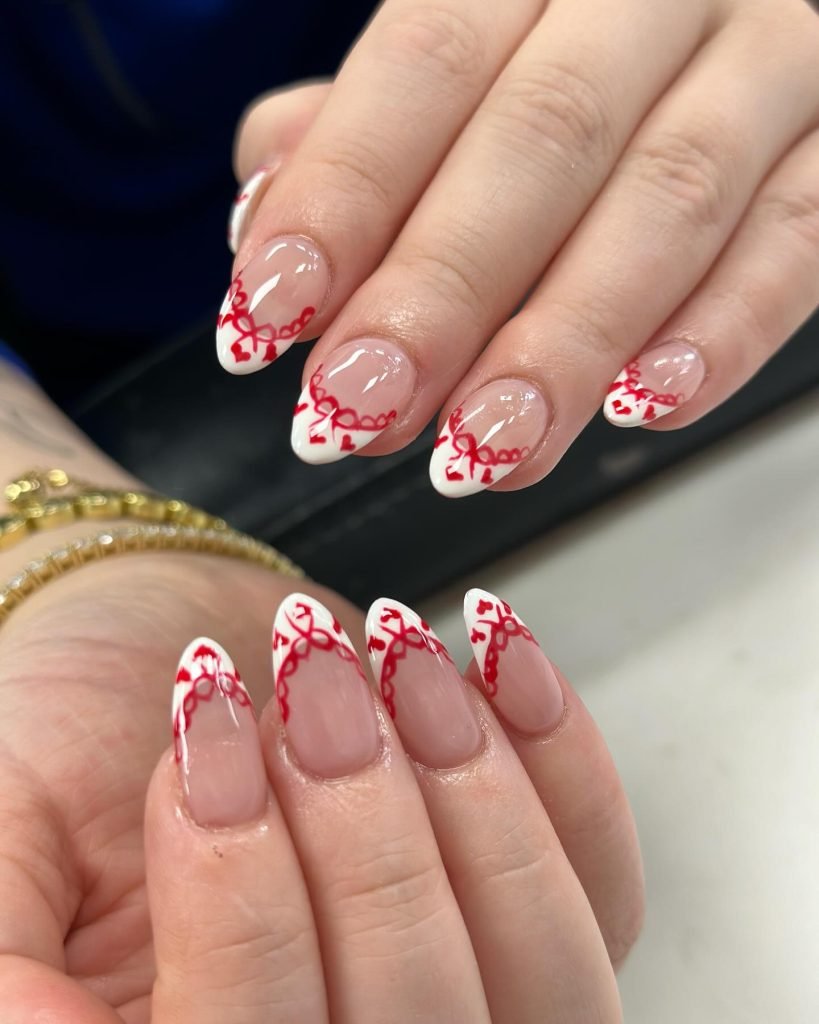 Elegant red and white nail art design with intricate patterns on almond-shaped nails.