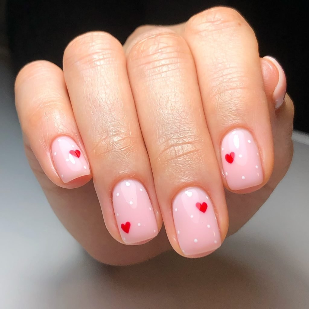 Pink manicure with red heart accents and white polka dots on nails. Perfect for a cute, romantic look.