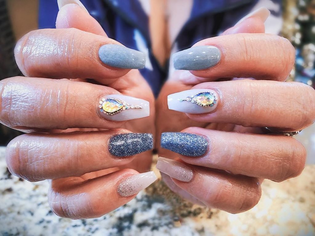 Elegant blue and gray nail art with gemstones and glitter, showcasing manicure design creativity and trends.