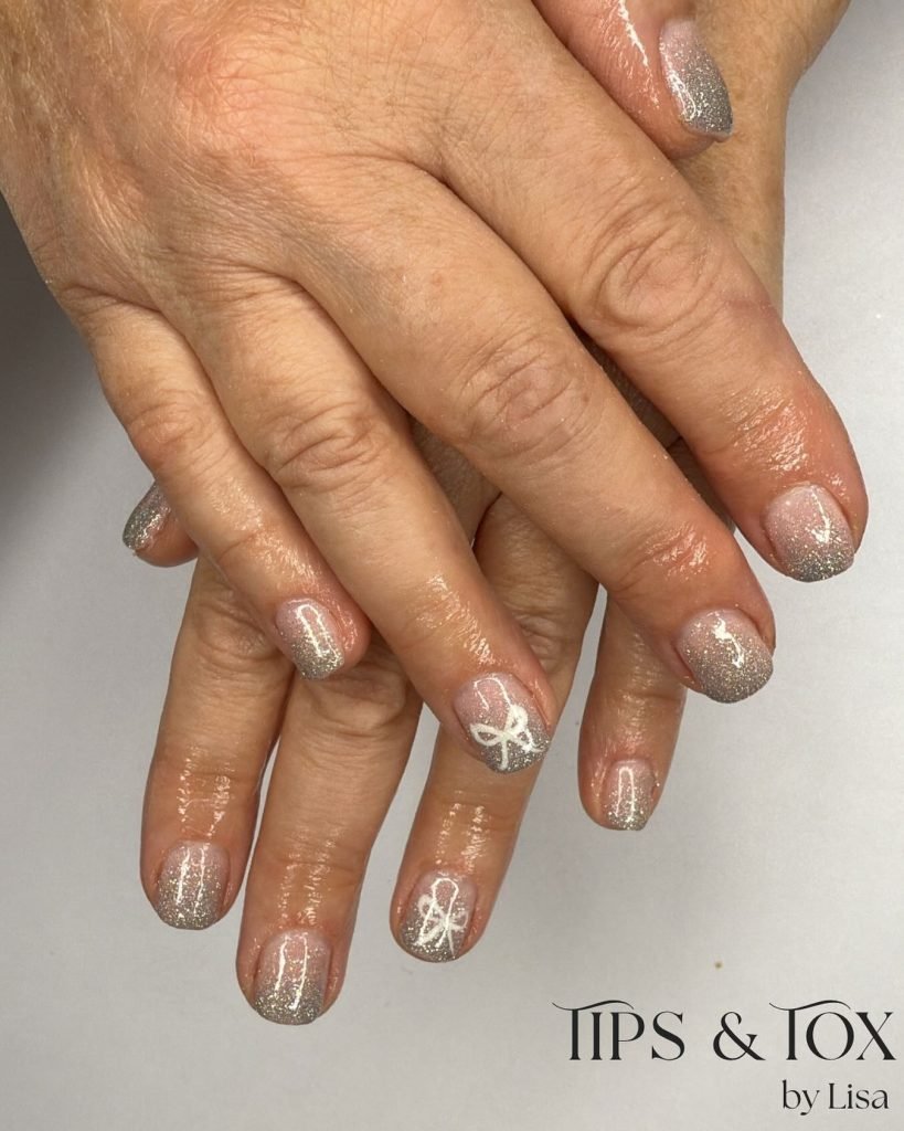 Silver glitter nails with white bow design on two fingers at Tips & Tox by Lisa. Perfect festive manicure.