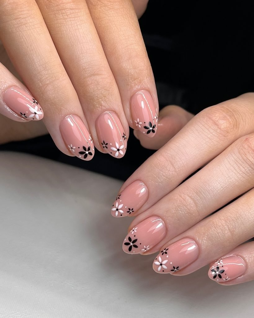 Close-up of pink nails with black and white floral designs. Trendy nail art for elegant and modern manicures.