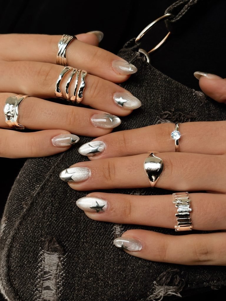 Silver star nail art with multiple rings on hands, holding a textured black bag.