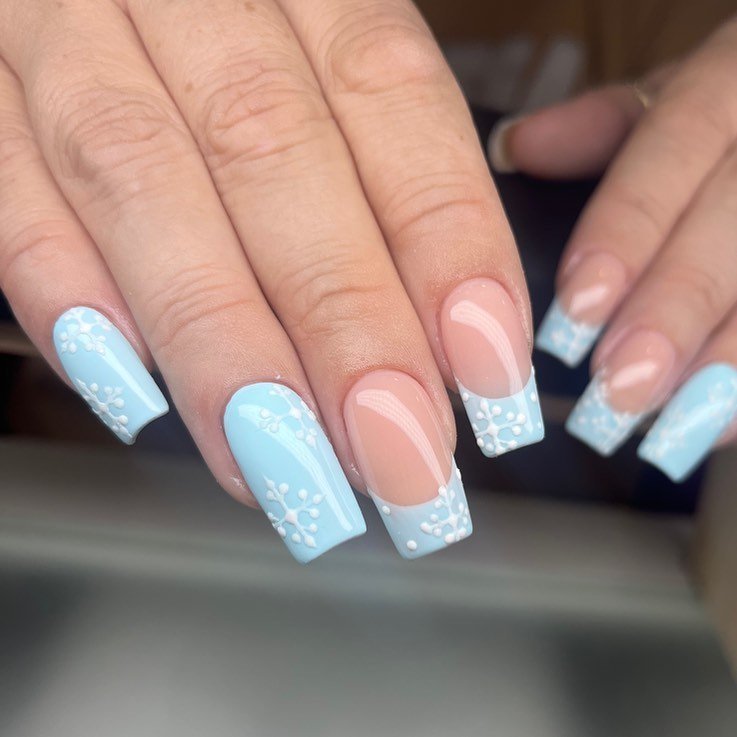 Light blue and nude French tip nails with delicate white floral design. Trendy manicure style for elegant looks.