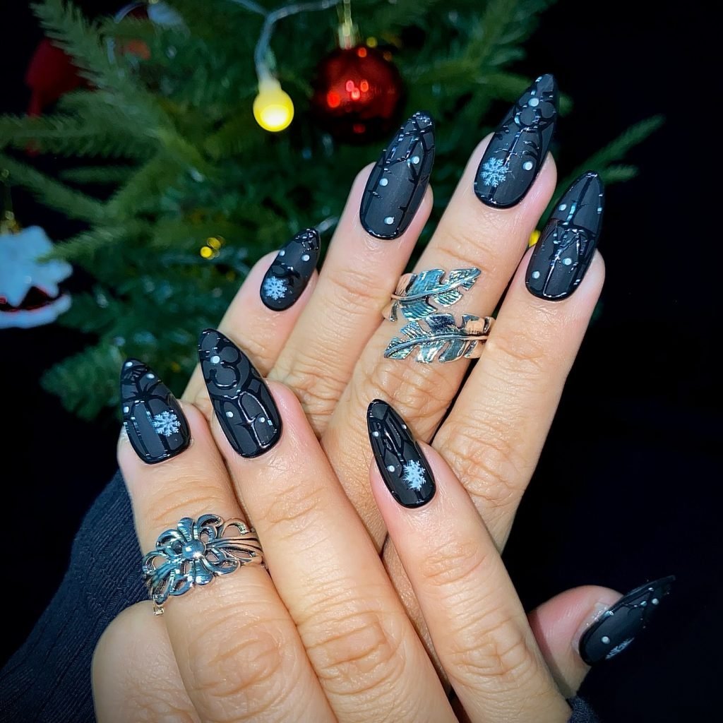 Elegant black Christmas nail art with snowflake designs, silver rings, and a festive background.