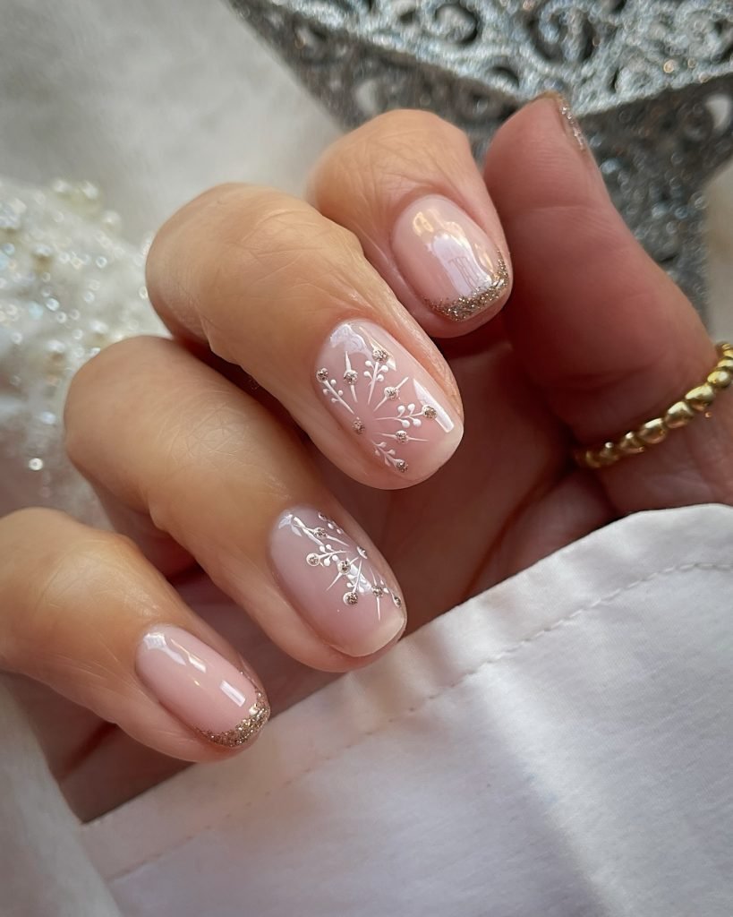 Elegant hand with glossy pink nails featuring white floral designs and subtle gold tips.