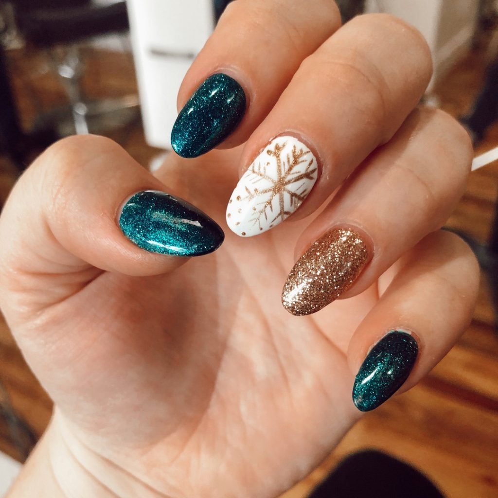 Festive manicure with teal glitter, gold sparkle, and snowflake design on oval-shaped nails.