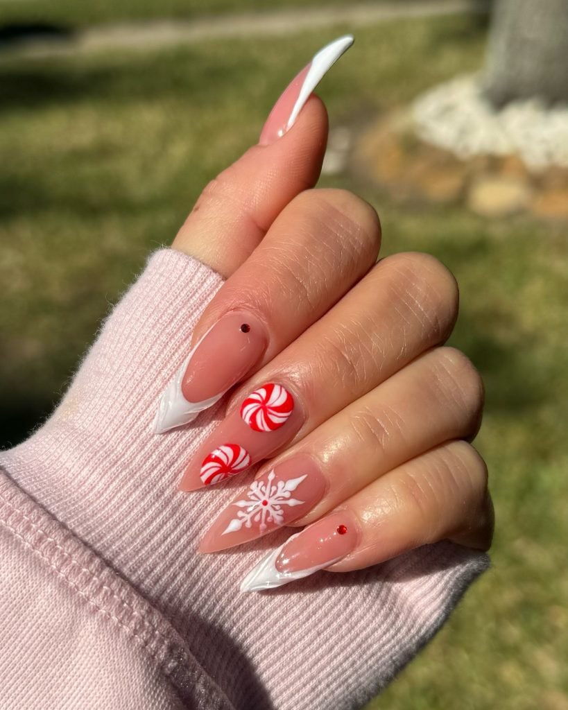Festive nails with red peppermint swirls, white snowflake, and rhinestone on a pink sweater background.