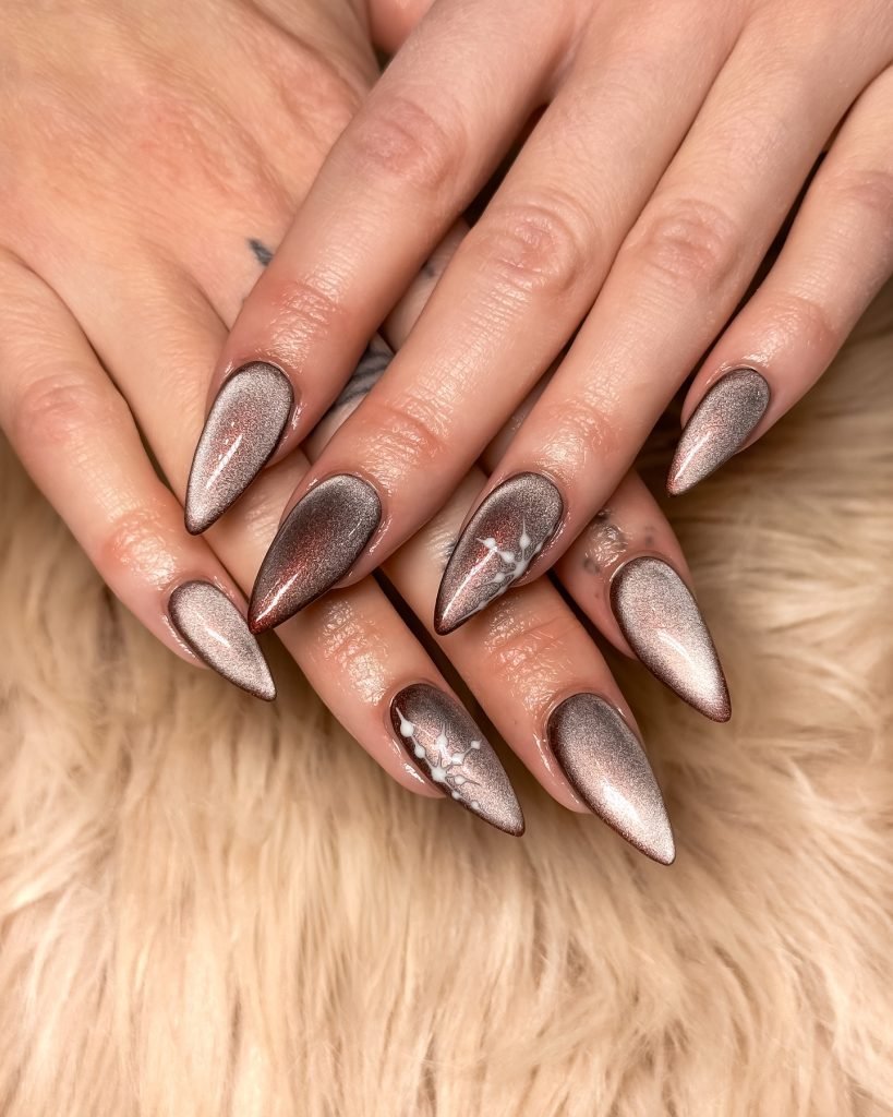 Stiletto nails with metallic brown polish and white accents on a soft fur background. Perfect for nail art inspiration.