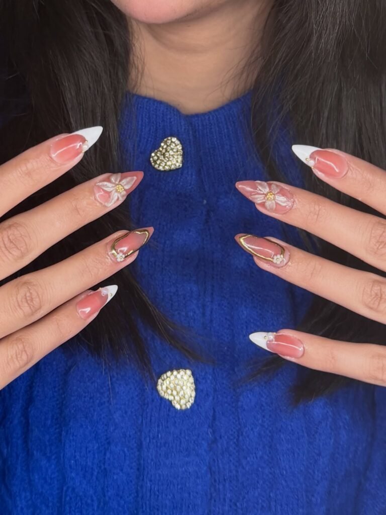 Stylish floral nail art on almond-shaped nails, complemented by a blue sweater with heart embellishments.