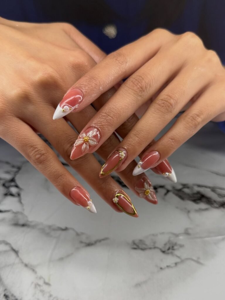 Elegant stiletto nails with floral design and white tips on marble surface. Fashionable 3D nail art.