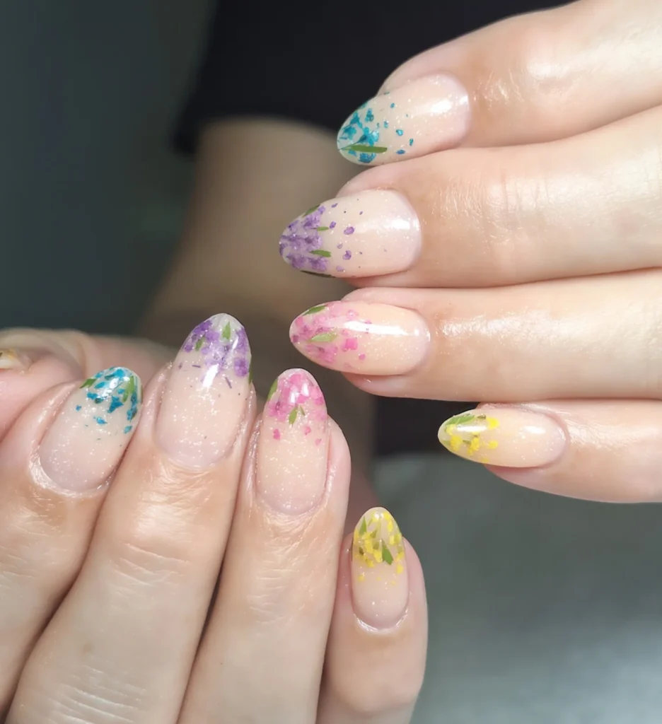 Colorful floral nail art with pastel shades and glitter on oval-shaped nails.