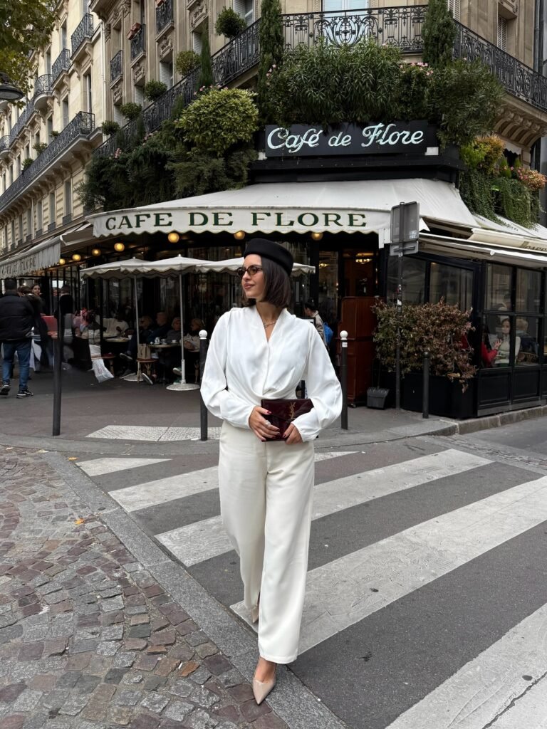 Woman in white outfit crossing street at Café de Flore, Paris, wearing beret, holding clutch.
