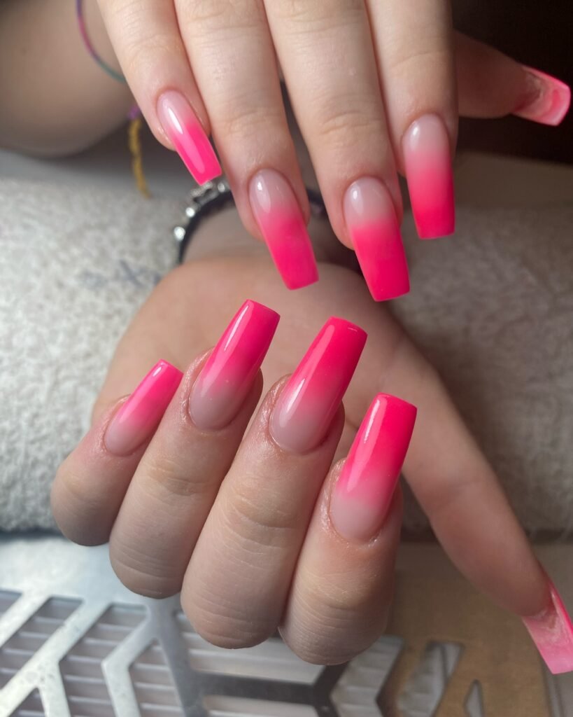 Bright pink ombre acrylic nails with a glossy finish on a white towel background.