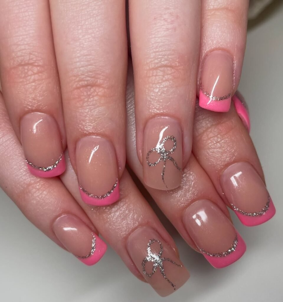 Nails with pink tips, silver glitter lines, and bow designs. Elegant and stylish manicure close-up.