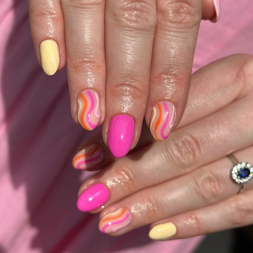 Colorful nail art with pink, yellow, and swirl designs on manicured hands, featuring a blue gemstone ring.