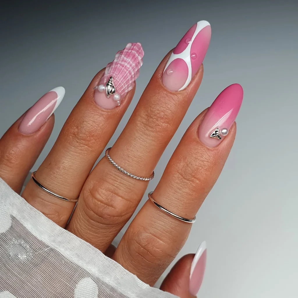 Stylish pink and white nail art with seashell and pearl accents on manicured hand wearing silver rings.