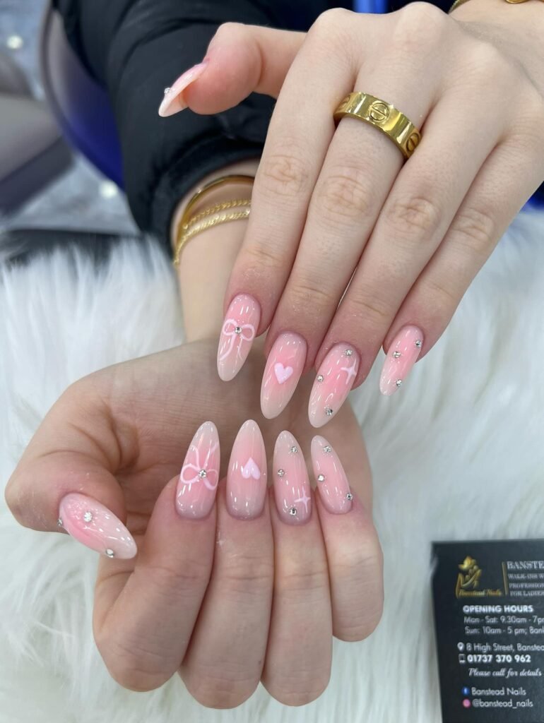 Elegant pink nails with heart and bow designs, showcasing trendy nail art on a soft, furry background.