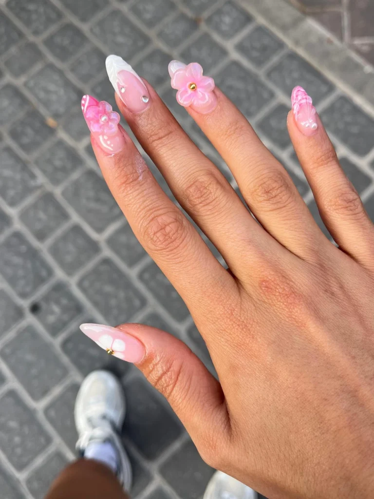 Hand with stylish pink floral nail art holding fingers open on a gray brick pavement background.