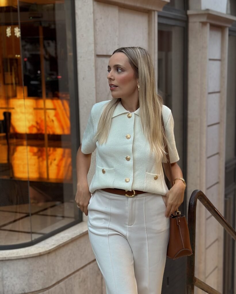 Stylish woman in white outfit with brown bag standing near boutique window, urban fashion scene