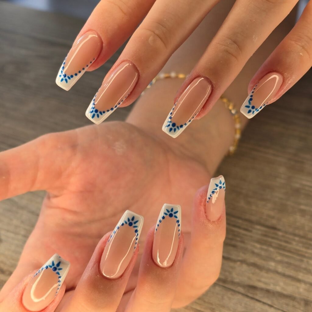 Elegant nude nails with blue floral French tips on a wooden table background.