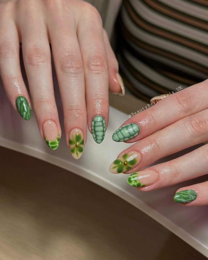 Green leaf nail art on hands over striped shirt backdrop, showcasing intricate designs and glossy finish.