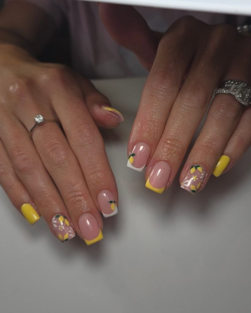 Stylish lemon-themed nail art with yellow accents, floral designs, and glossy finish on manicured hands.