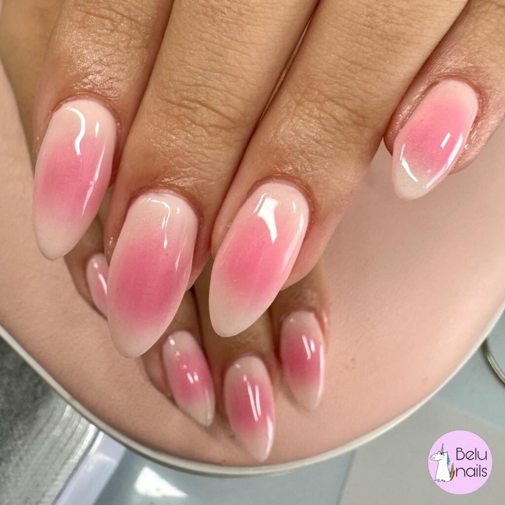Pink ombre almond-shaped nails with a glossy finish, close-up. Stylish and trendy nail art design.