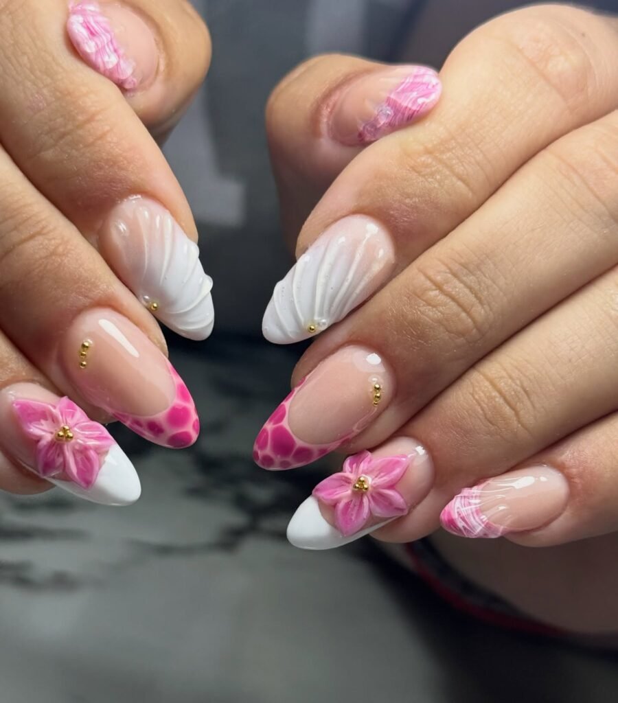 Colorful floral and abstract nail art with pink, white, and gold accents on almond-shaped nails.