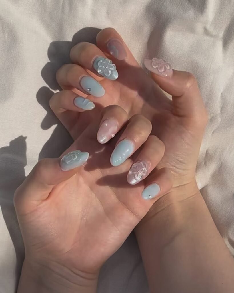 Pastel blue and pink manicure with floral 3D nail art on hands, photographed on a light background.