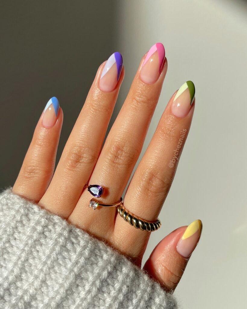 Colorful geometric nail art with pastel shades on a hand wearing stylish rings and a cozy sweater.