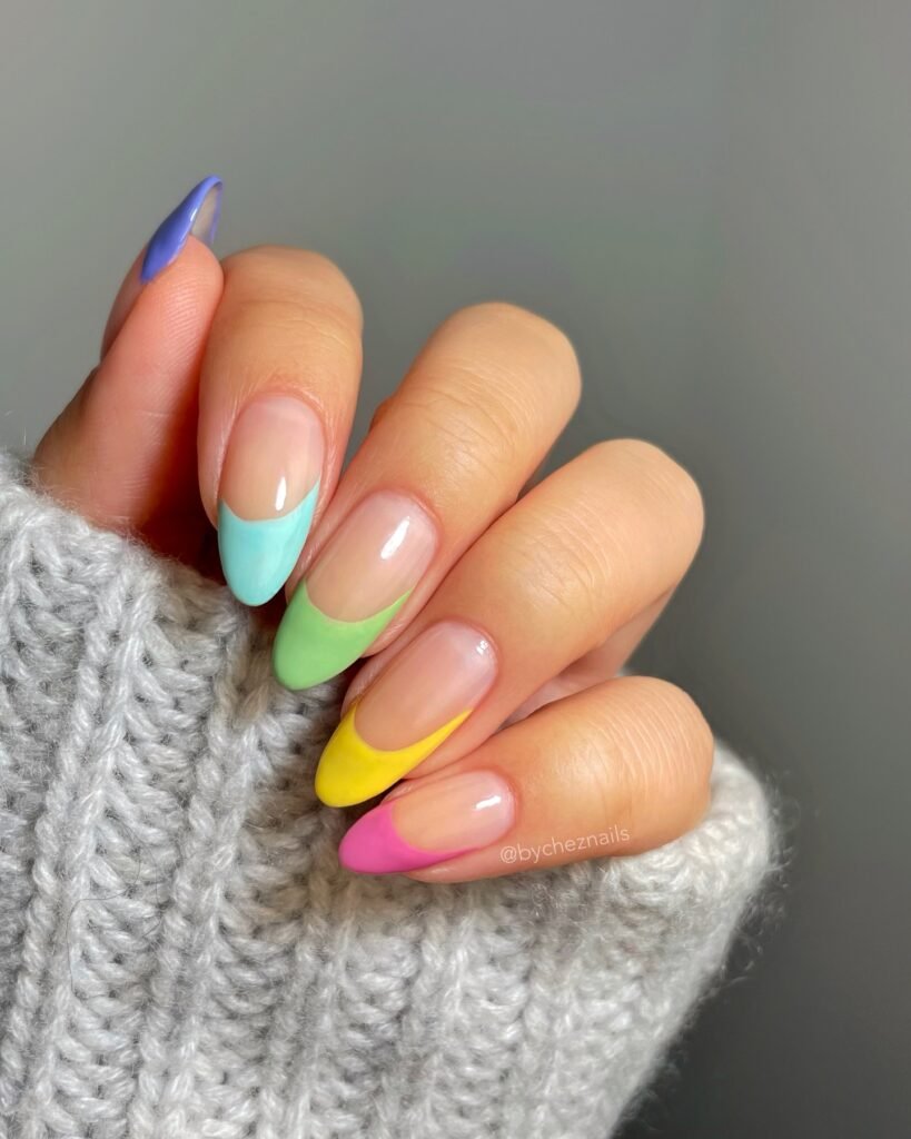Colorful pastel French manicure on almond-shaped nails against a cozy gray sweater background.