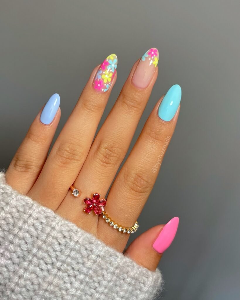 Colorful floral nail art showcasing pastel blue, pink, and yellow designs with a cozy sweater and elegant pink ring.