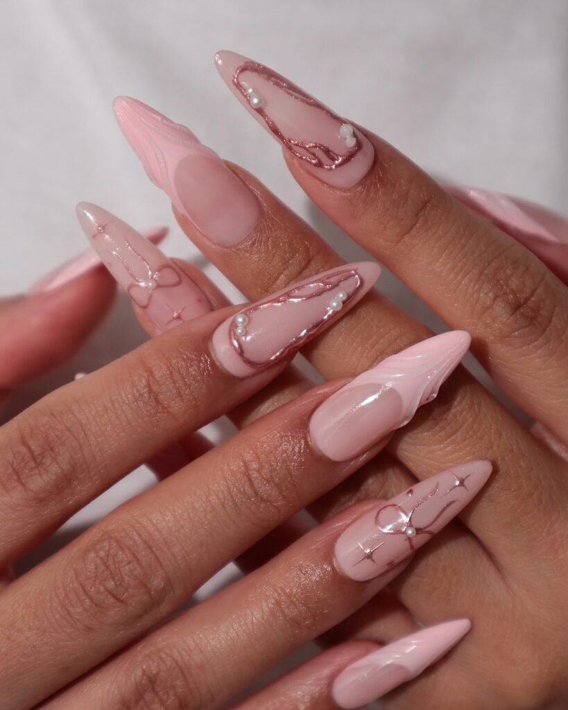 Elegant pink stiletto nails with intricate designs and pearl accents for a chic manicure look.