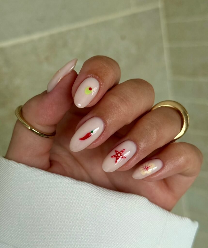 Close-up of hand with elegant nail art featuring small food and star designs, accessorized with gold rings.