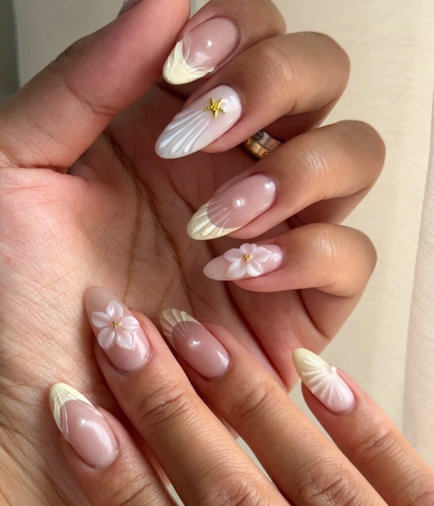 Elegant nail art with floral designs, pearls, and gold accents on a hand with almond-shaped nails.