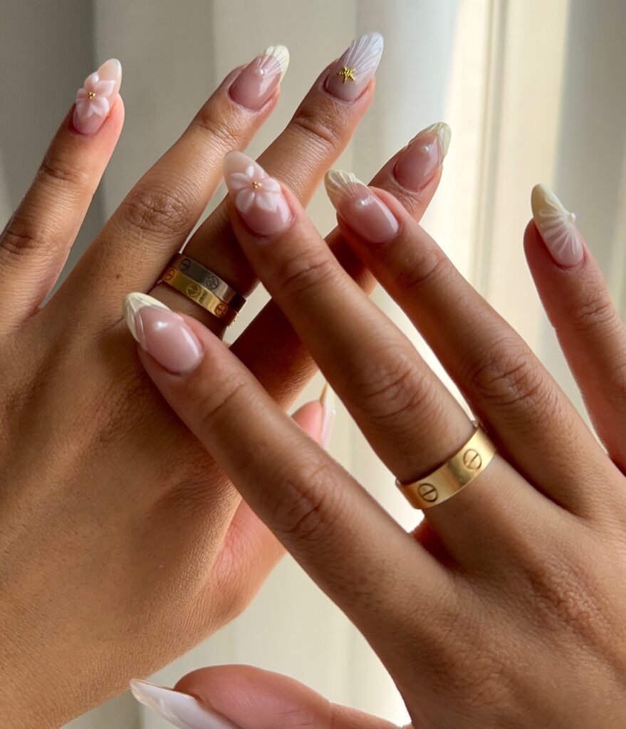 Elegant floral nail art design with gold rings on manicured hands.