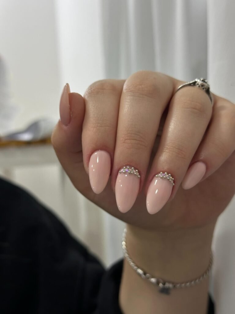 Elegant almond-shaped nails with pink polish, adorned with rhinestones, showcasing chic manicure style.