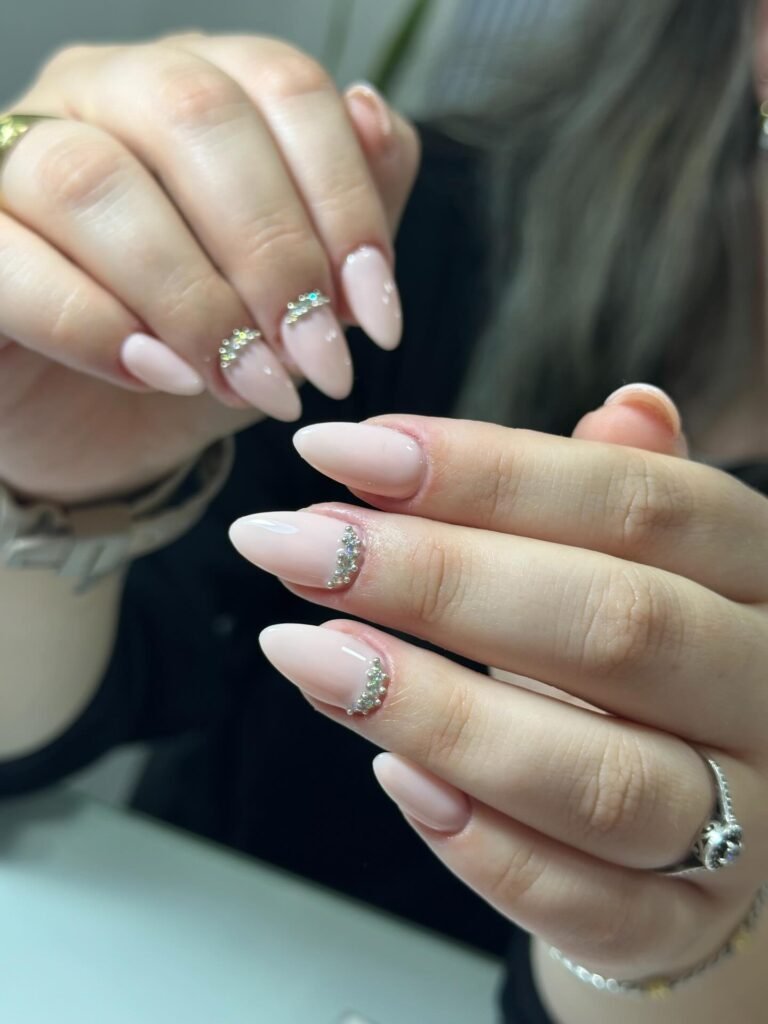 Elegant almond-shaped nails with pale pink polish and rhinestone accents on a woman's hands.