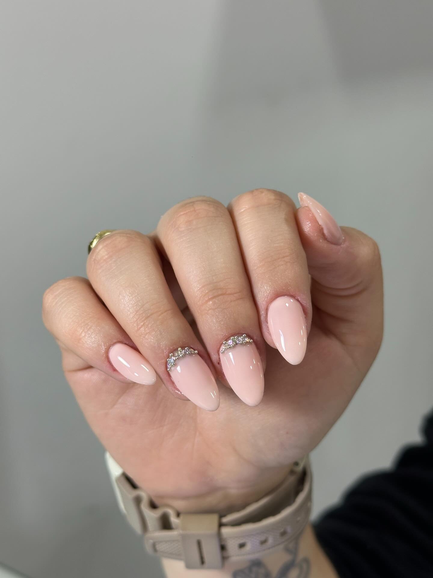 Manicured hand with light pink nails and rhinestone accents on almond-shaped tips.