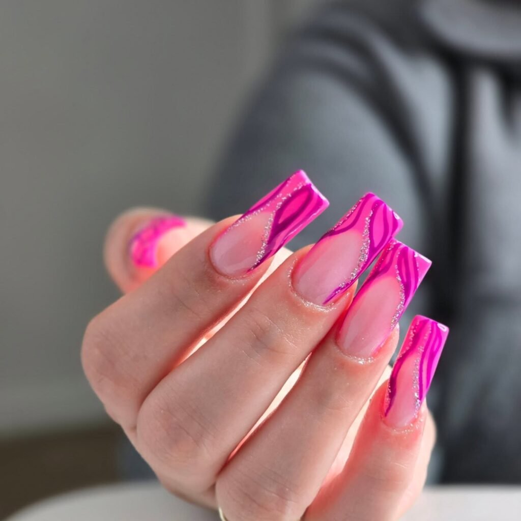 Pink and purple acrylic nails with wavy, glitter design on female hand.