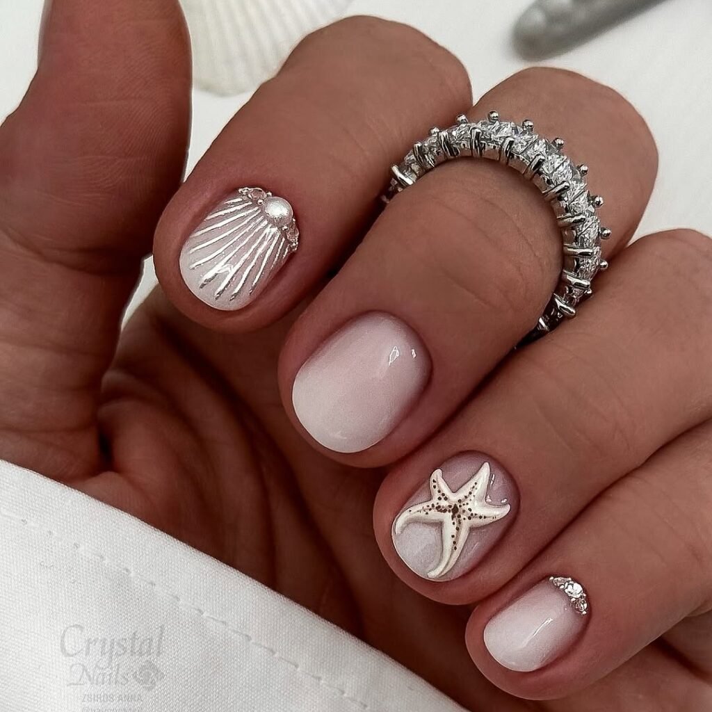 Elegant seashell and starfish nail art with silver accents, featuring a sparkling ring on manicured fingers.