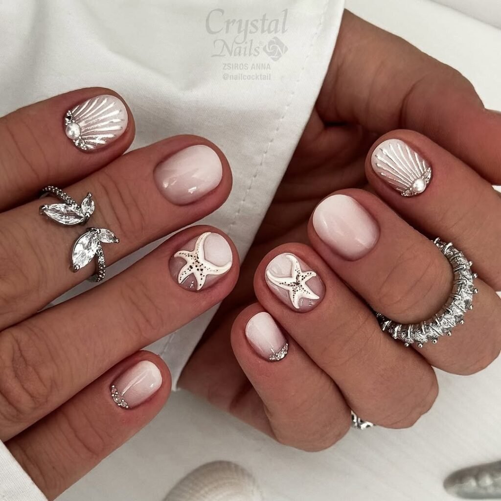 Elegant seashell and starfish nail art with silver rings, displaying intricate ocean-themed designs on manicured nails.