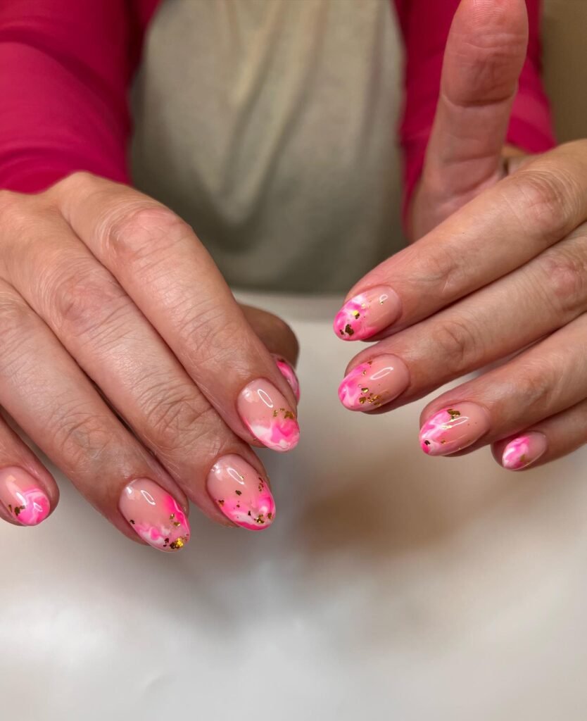 Pink floral nail art with gold accents displayed on manicured hands against a neutral background.